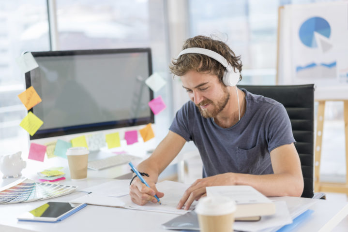Young graphic designer working at the office and listening to music wearing headphones